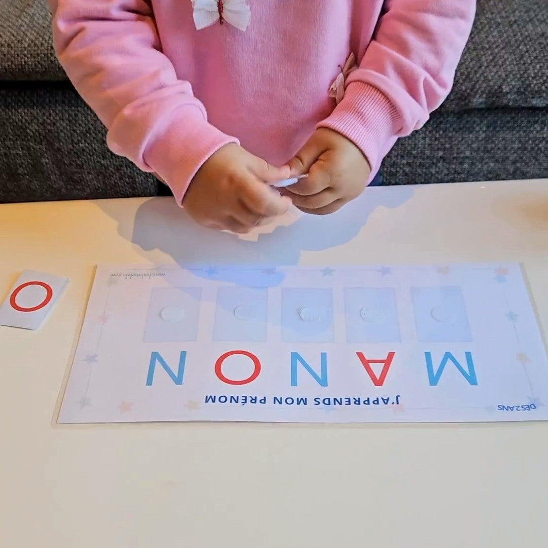 Une petite fille scratche les lettres de son prénom MANON sur le plateau J'apprends mon prénom