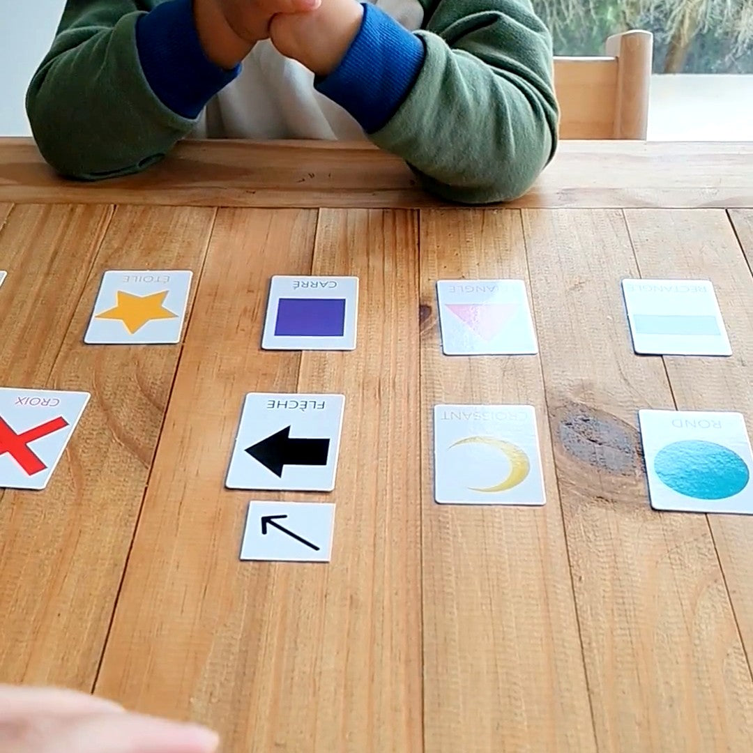 Cartes des formes géométriques posées sur la table devant un enfant : étoile, carré, triangle, croix, flèche, croissant, rond